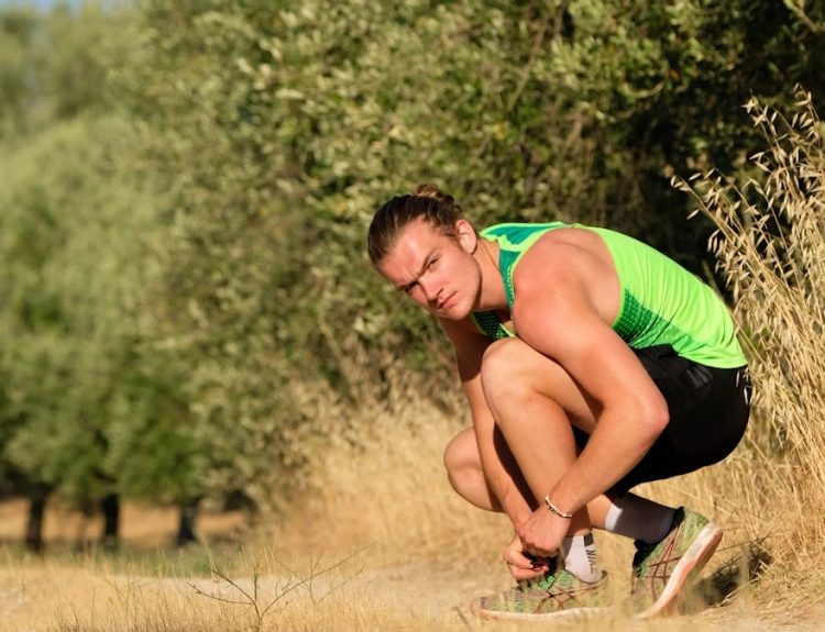a man squatting down in a field with trees in the background
