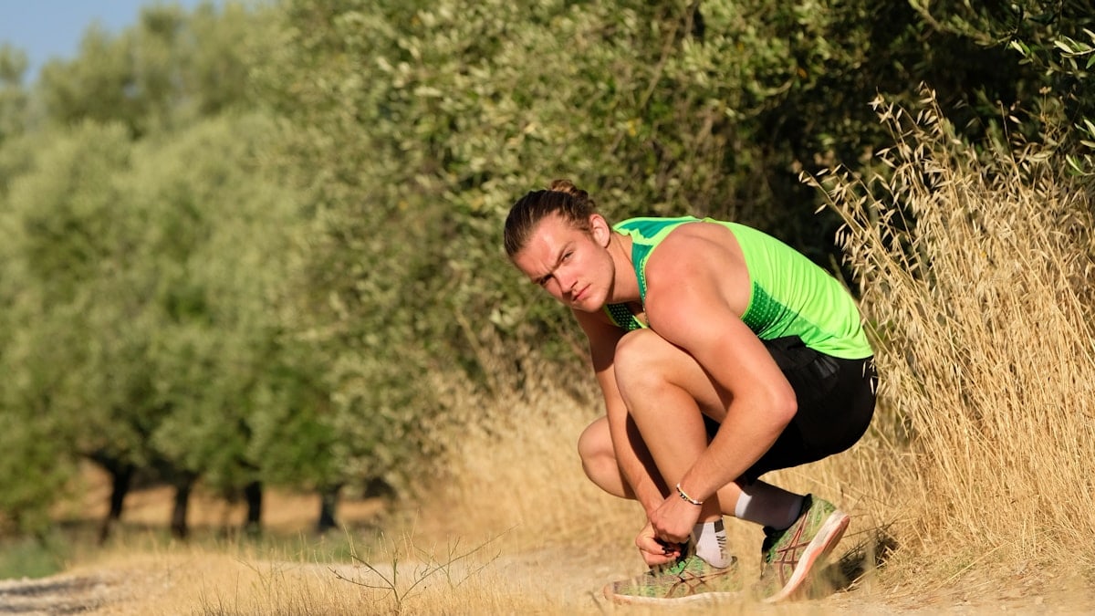 a man squatting down in a field with trees in the background